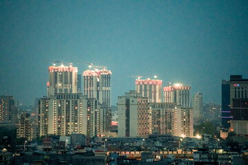 Fototapeta premium modern Gurgaon cityscape at dusk featuring illuminated residential towers, commercial skyscrapers, and urban development under a blue evening sky in Delhi