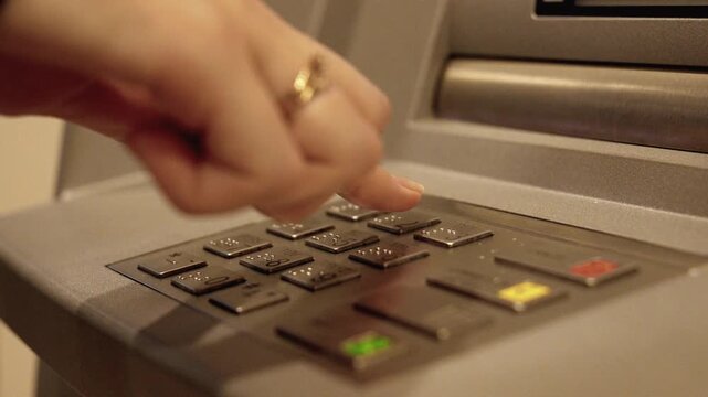 Close-up shot of a female hand entering a secret pin code on the keypad of an automated teller machine to access her bank account and withdraw money for financial transactions