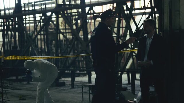Policeman and detective investigating murder at industrial plant crime scene