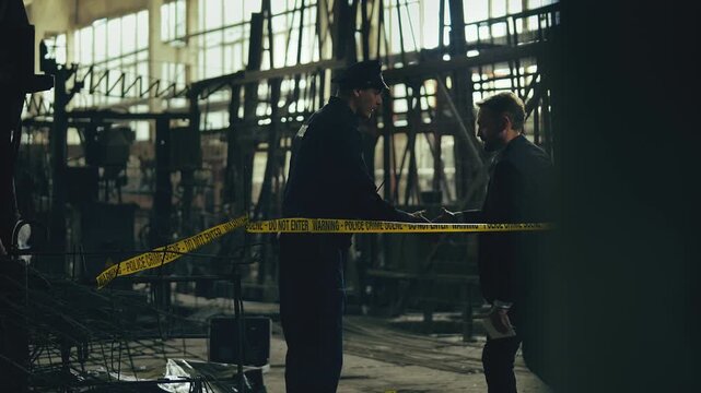 Detective arriving at industrial plant crime scene, speaking with police officer