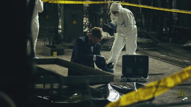 Detective putting on gloves before examining body bag at industrial crime scene