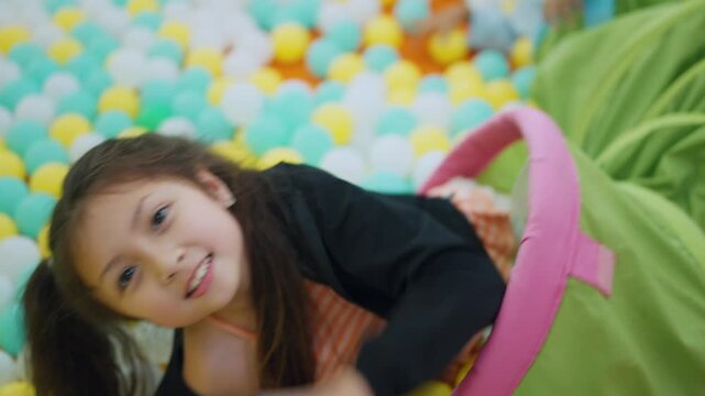 Joyful Dive into a Ball Pit: A young girl with a beaming smile dives into a vibrant ball pit, surrounded by a sea of colorful spheres, embodying pure childhood delight and playful energy.