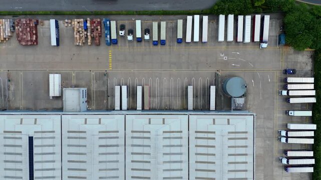 Aerial view of commercial warehouses with parked semi-truck trailers and loading bays at a logistics facility in Kettering, England, United Kingdom.