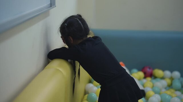 Isolated Child in Playroom: A young child sits alone in a colorful playroom filled with toys. The scene evokes feelings of sadness, loneliness, and neglect.
