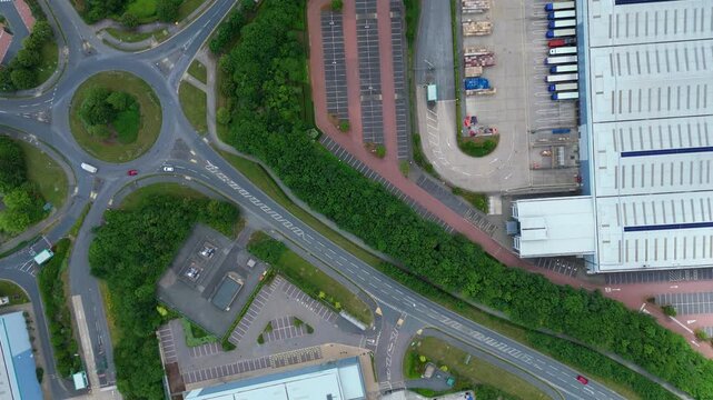 Aerial view of commercial warehouses with loading bays, parking lots, and a roundabout in Kettering, England, United Kingdom.