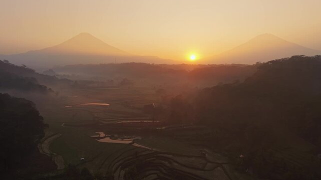 Aerial view of terraced rice fields at sunrise with distant mountains and morning mist in Selomerto, Central Java, Indonesia.