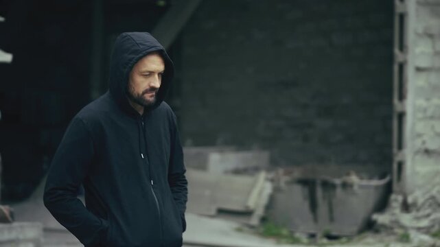 Man in hoodie walking alone through abandoned industrial site, crime concept