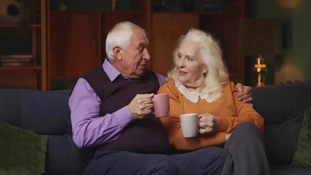 Happy elderly couple drinking tea and hugging at home, spending time together