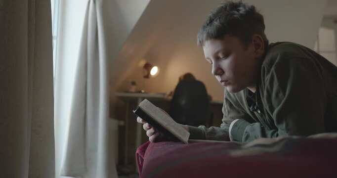 Caucasian Boy Kid Read Bible Book Lying on Bed in Bedroom. 4K 10-bit