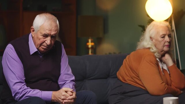 Sad elderly man and woman sitting apart on sofa, relationship problems