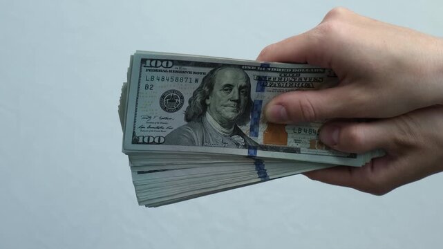 Hand grips a stack of hundred-dollar bills. Fingers steady, holding cash tightly. Money's value implied by crisp, clean bills.