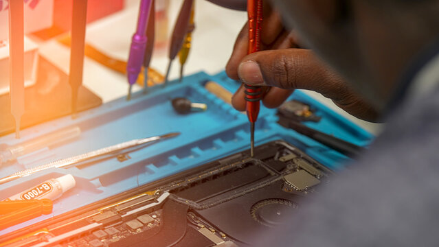 Technician repairing laptop close-up in electronics workshop with tools and components