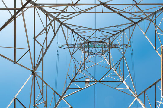 Low-angle shot of a high-voltage transmission tower against a clear bright blue sky