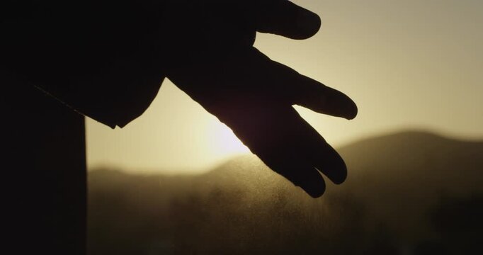 Silhouette hand spread ash at outdoor mountain sunset nature as peaceful farewell memory concept for grief background