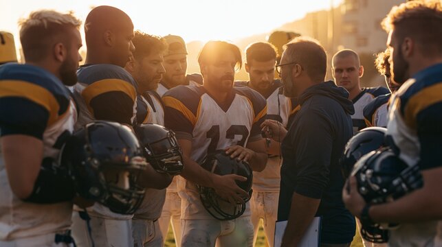 A group of athletic players gathers in a tight huddle after a passing drill, helmets tucked under arms, coach correcting footwork with a whistle and clipboard. Sunlit practice field, tackle dummies
