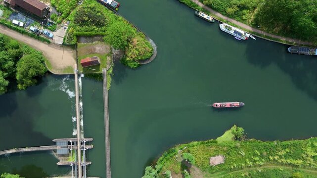Aerial view of Feildes Weir Lock with narrowboats navigating the canal, lush green banks, and calm water in Hoddesdon, England, United Kingdom.