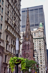 Fototapeta premium Trinity Church Gothic Revival brownstone spire and clock tower rising between modern skyscrapers and historic buildings on Broadway, Lower Manhattan, New York City, USA
