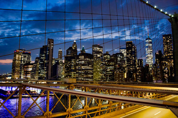 Lower Manhattan illuminated skyline with One World Trade Center seen through Brooklyn Bridge steel cables and truss structure at dusk, New York City, USA © AMTravelPhotographer