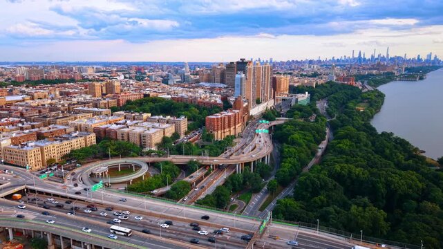 Lively highways along the green waterfront of the Hudson River. Dramatic clouds gathered in the sky over the cityscape. Aerial view.