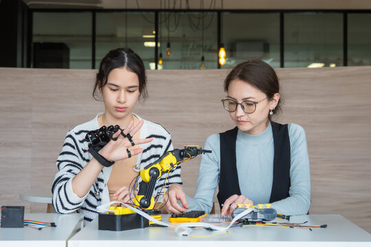 Expert female mentor teaching young student robotic coding on laptop; diverse women collaborating on STEM education project fostering future innovation and learning modern classroom setting.