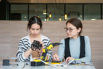 Fototapeta premium Expert female mentor teaching young student robotic coding on laptop; diverse women collaborating on STEM education project fostering future innovation and learning modern classroom setting.