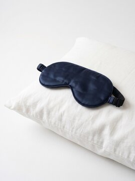 A deep navy blue velvet sleep mask rests on a clean white linen pillow, suggesting comfort and rest