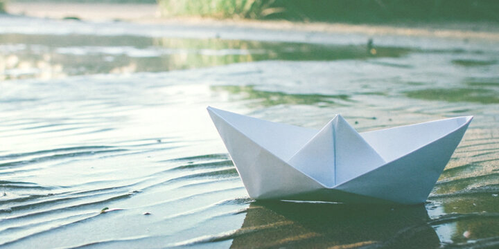 Fresh start and setting off with a white paper boat floating on the shallow water