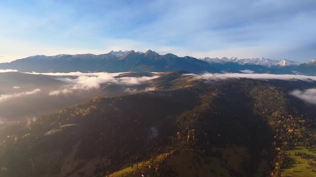 Osturna, Slovakia - 4K Aerial view of the High Tatras Mountain range on a sunny, cloudy autumn morning. Warm colors, autumn foliage, blue sky