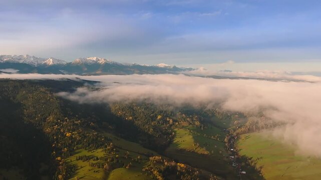 Osturna, Slovakia - 4K Aerial view of the High Tatras Mountain range on a sunny, cloudy autumn morning. Warm colors, autumn foliage, blue sky