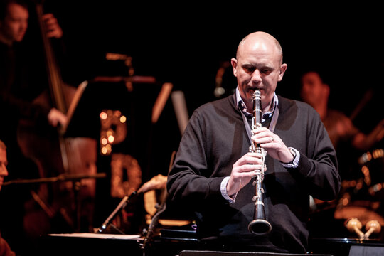 Clarinet soloist. A clarinet player performing a solo in front of a big band on a dark concert stage.