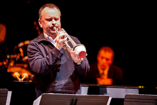 Live trumpet solo. A big band trumpeter playing a solo with a cup mute on a dark concert stage during a jazz performance.