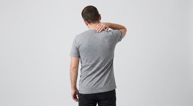 Adult man experiencing upper back pain and neck stiffness, rear view, hand pressing painful area on upper back, healthcare and body pain concept, realistic human posture, gray t-shirt, clean studio