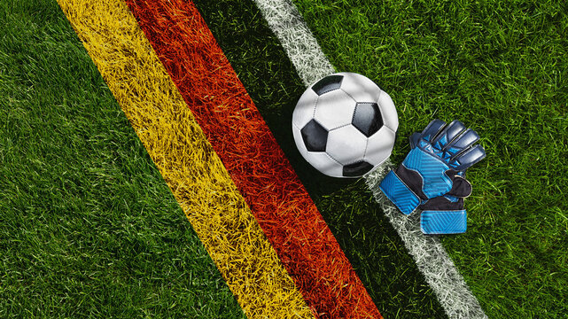 green grass texture with a soccer ball and goalkeeper gloves with the German flag - well-groomed turf. Banner with copy space.