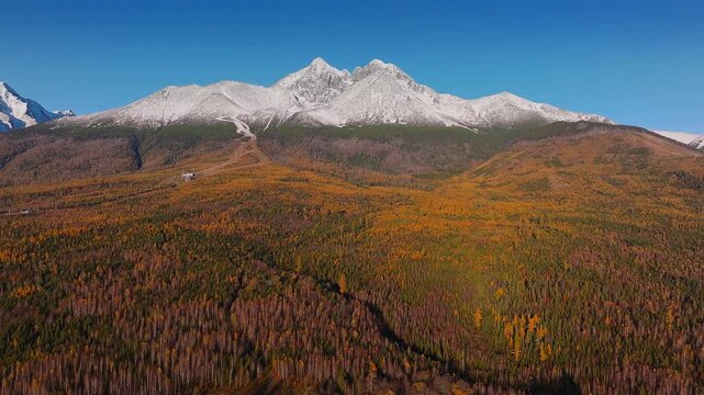 High Tatras, Slovakia - 4K Flying away the snowy High Tatras Mountain range near Strbske Lake (Strbske Pleso) on a sunny autumn afternoon with warm colors, autumn foliage and blue sky