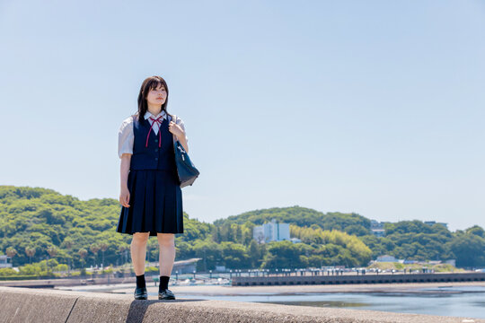 海辺の防波堤を歩く女子高校生と夏の青空