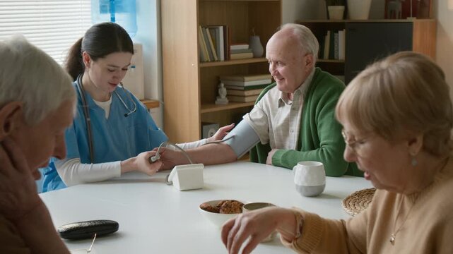 Senior couple playing chess while female nurse measures blood pressure of senior man in retirement home. Clip suitable for senior care and assisted living facility marketing