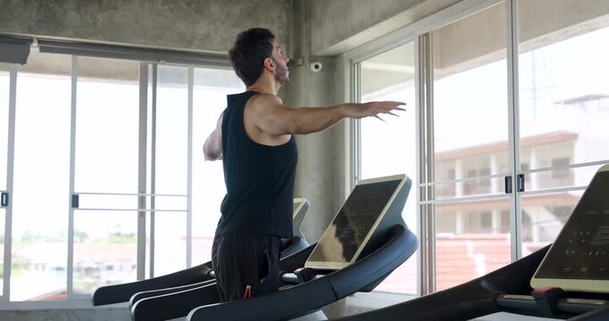 Adult Caucasian man walks on treadmill while swinging arms for warm up in modern gym. Male athlete prepares cardio running routine, mobility exercise, endurance training, healthy lifestyle goal.