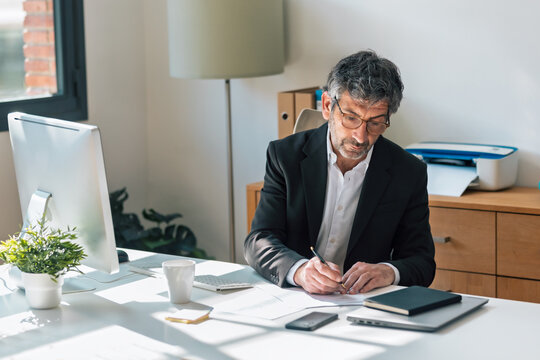 Mature elegant businessman working on a computer while taking notes in the office