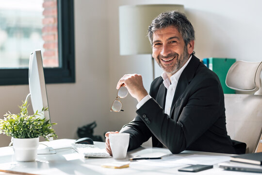 Smiling elegant businessman working on a computer while looking at camera in the office