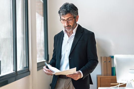 Elegant businessman reading some notes while standing next to the window at the office.
