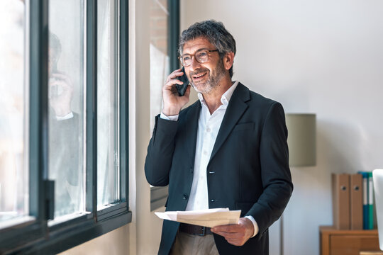 Elegant businessman reading some notes while talking with smartphone standing  at the office.