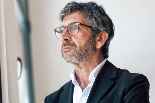 Elegant handsome businessman thinking while looking forward standing next to the window at the office.