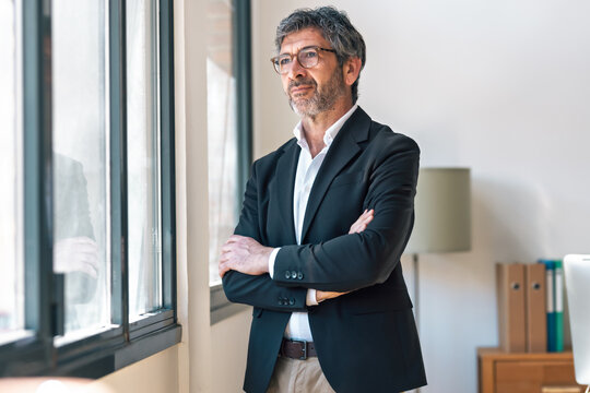 Elegant handsome businessman thinking while looking forward standing next to the window at the office.