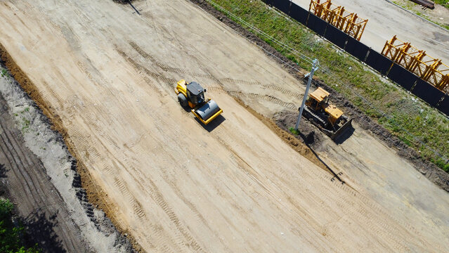 Yellow road roller compacting a dirt road bed at an infrastructure construction site