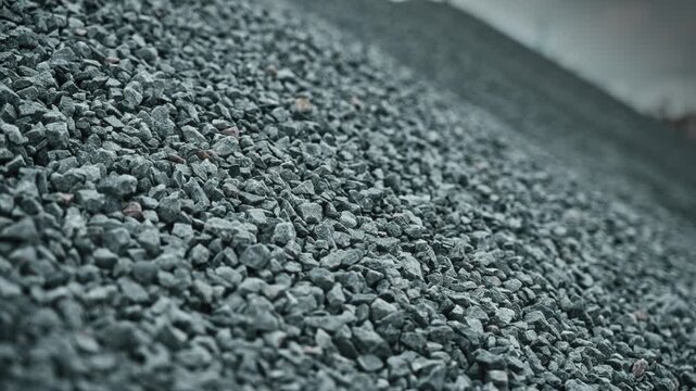 Diagonal slope of crushed gray stone stockpile for construction aggregate, showing rough angular texture, industrial scale, low viewpoint, muted overcast light, and broad surface detail