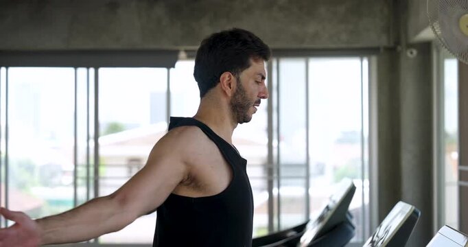 Side view of adult Caucasian man walking on treadmill while swinging arms for shoulder warm up in modern gym. Male athlete prepares cardio routine, mobility exercise, healthy fitness lifestyle.