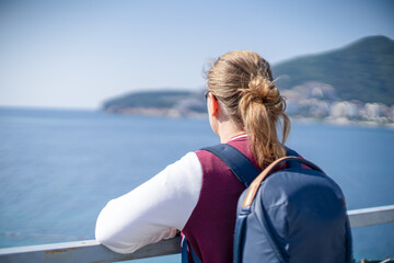 Fototapeta premium Woman standing from behind on a boat deck looking at a scenic sea bay with mountain in the distance, travel lifestyle, summer vacation.
