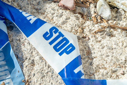Blue STOP barrier tape wrapped around rock and shell on a stony beach, caution concept, restriction and safety theme