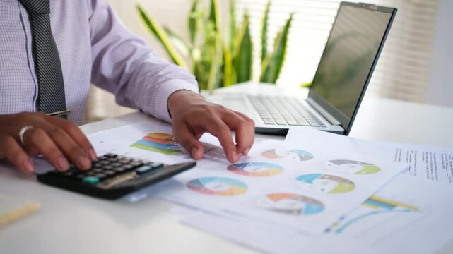 Close up view of accountant engaged in financial calculations and data analysis, using calculator reviewing documents, charts, and graphs. Accounting, analytics, budgeting, investments evaluation. 