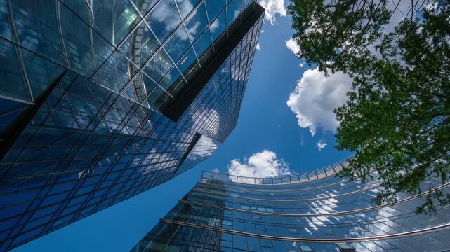 Low angle wide shot time-lapse of downtown high-rise glass skyscrapers on sunny day, financial district looking up tall modern architecture office buildings city center street, blue sky white clouds